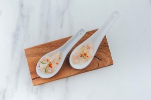 Zwei chinesische Löffel auf einem Holzbrett mit einem Stück Fisch jeweils