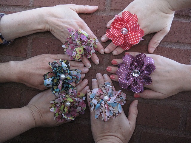 die rechten Hände von sechs verschiedenen Frauen auf einer Wand jede trägt einen großen Blumenstoffring mit einer Perle in der Mitte