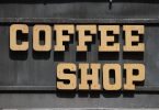 geschrieben steht coffee shop in beigen Großbuchstaben an einer dunklen Wand