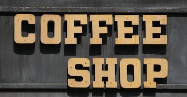 geschrieben steht coffee shop in beigen Großbuchstaben an einer dunklen Wand