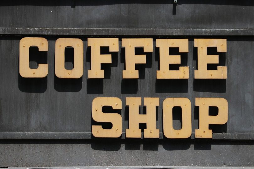 geschrieben steht coffee shop in beigen Großbuchstaben an einer dunklen Wand
