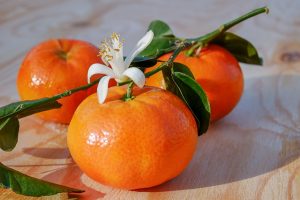 drei Mandarinen auf einem Holztisch mit Blättern und einer Blüte