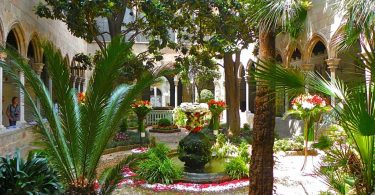 der Innenhof einer Kathedrale mit einem Blumengeschmückten kleinen Springbrunnen in der Mitte