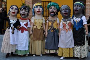 sechs Dickköpfe, ein Bauernpärchen, ein Adelspärchen und ein farbiges Pärchen, wobei alle Herren lange Kleider mit Schütze tragen