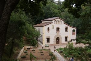 ein älteres Bauernhaus das mitten im botanischen Garten steht, es ist weiss gestrichen und hat unten zwei groe eckige Fenster und oben mehrere kleine gewölbte Fenster