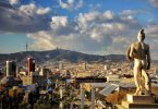 Aussicht auf Barcelona von Montjuïc aus, man sieht eine der Statuen des Nationalmuseums und ein blauer Himmel mit einigen weißen Wolken