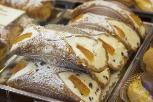 Vitrine einer Bäckerei mit einem frittiertem Gebäck das mit Sahne, Rosinen und Orangenkonfekt gefüllt ist