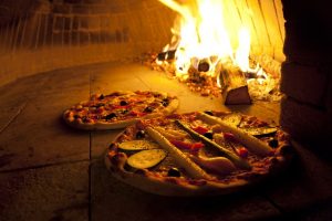das Innere eines Holzoffens mit zwei Pizzas und brennenden Holzscheiten darin
