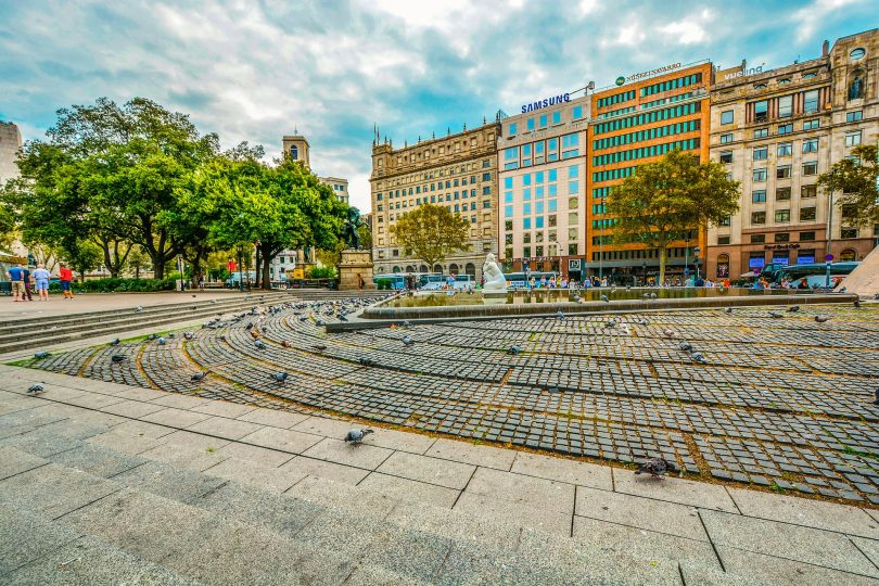 ein großer Platz in Barcelona mit Bäumen einem Springbrunnen und kreisförmig angelegte Pflastersteine