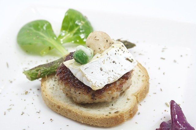 Zwieback mit einer kleinen Frikadelle, Camembert und Gemüse darauf