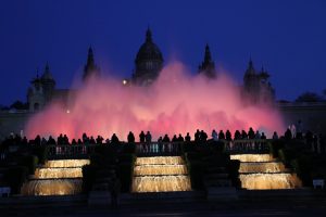 Das Wasserspiel scheint gerade ein rosaner Nebel zu sein, im Hintergrund ist der Palau zu sehen und davor weiss beleuchtete kleine Wasserfälle