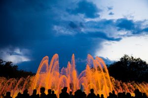 Orangenes Lichtspiel der Fontänen bei Dämmerung mit den Schatten der Zuschauer davor
