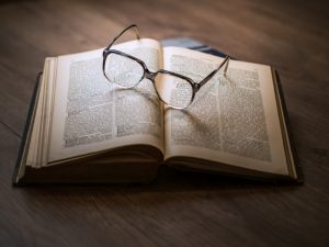 ein offenes Buch auf einem Holztisch mit einer Brille darauf