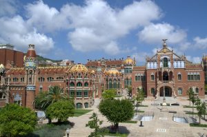 die Gebäudeanlage des Hospital de la Santa Creu i Sant Pau mit grünen Bäumen und Palmen im Vorhof