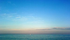 im unteren Teil des Fotos das grau-blaue Meer und darüber ein blau-orangener Himmel