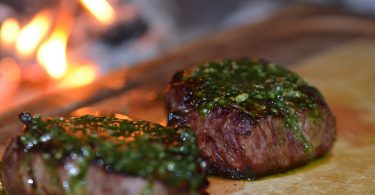 zwei saftig angebratene Steaks mit grünem chimichurri darauf