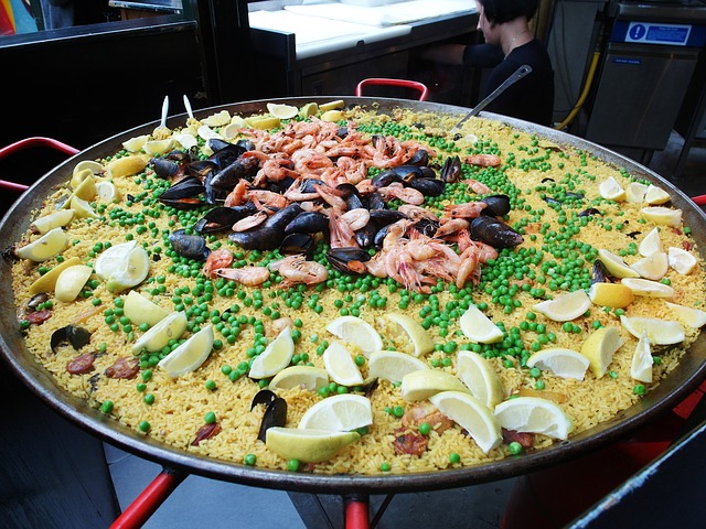 Eine große Paella in der traditionellen Pfanne mit vielen Zitronenstücken drumherum und in der Mitte Garnelen und Miesmuscheln