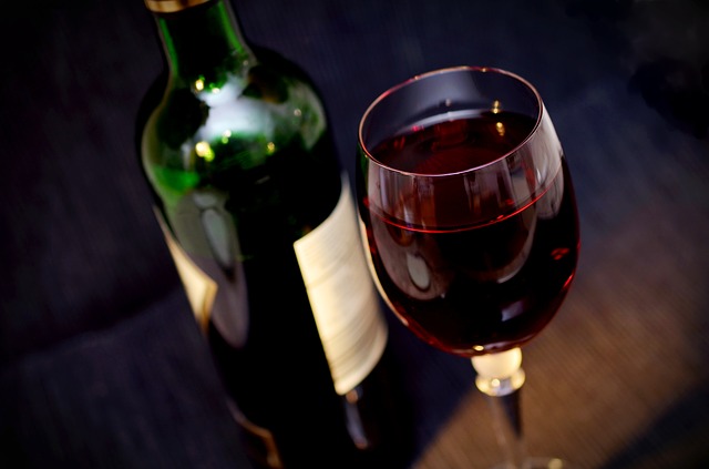 eine grüne Flasche Wein und ein volles Glas mit Rotwein die auf einem Holztisch stehen