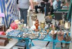 kleiner stand auf einem Flohmarkt, zum verkauf stehen kleine Antiquitäten wie Kerzenhalter und Bügeleisen
