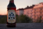 eine Flasche Moritz Bier die auf einer Mauer steht im Hintergrund Wohnhäuser im Licht des Sonnenuntergangs