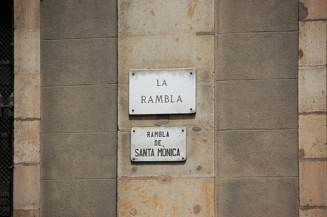 zwei Straßenschilder an der beigen Mauer eines Gebäudes, auf einem steht la Rambla und auf dem anderen Rambla de Santa Mònica