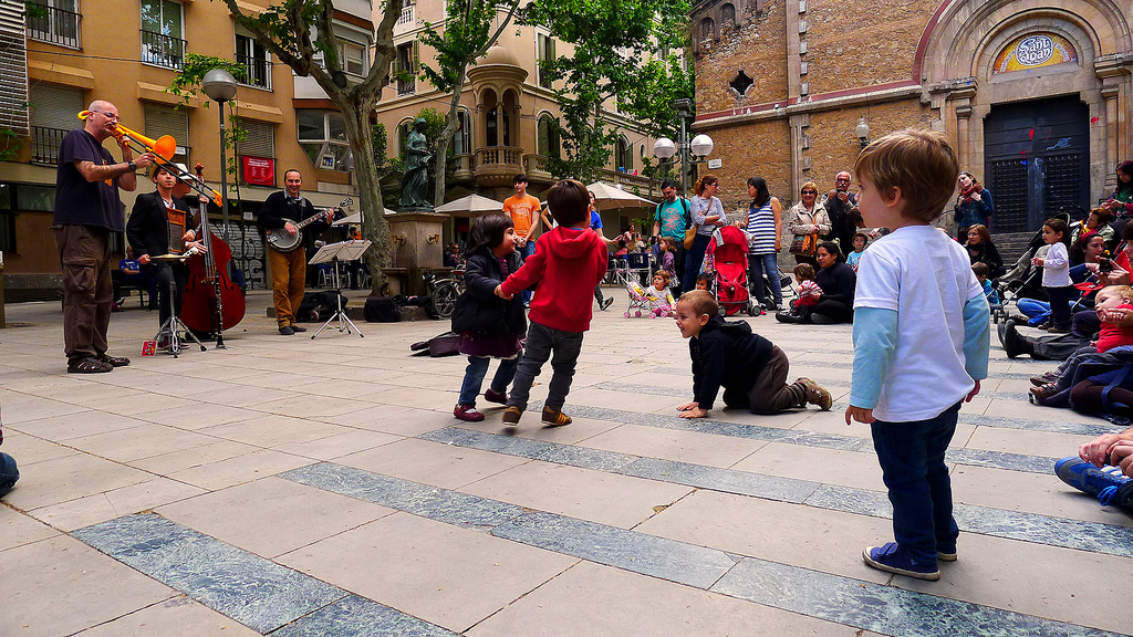 Mehrere Kinder die auf einem Platz im Stadtteil Gracia spielen, am Rand spiel eine Band