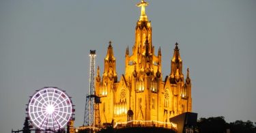 die große Kirche auf dem Tibidabo Berg beleuchtet bei Nacht und links daneben das Riesenrad des Vergnügungsparks