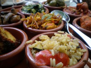 verschiedene Tapas in Tonschüsselchen wie Reis mit Gemüse, Tortilla, Paella, Fleisch in Tomatensauce