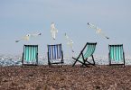 drei Strandstühle an einem Strand nebeneinander Gestell, drei grüne und ein blauer, mit vier Möwen die darüber fliegen