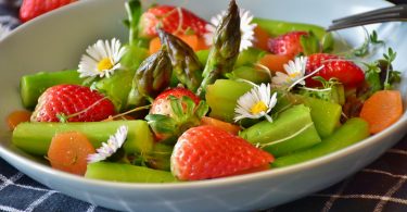 weisse Schüssel mit grünem Spargel, ganzen Erdbeeren und Gänseblümchen