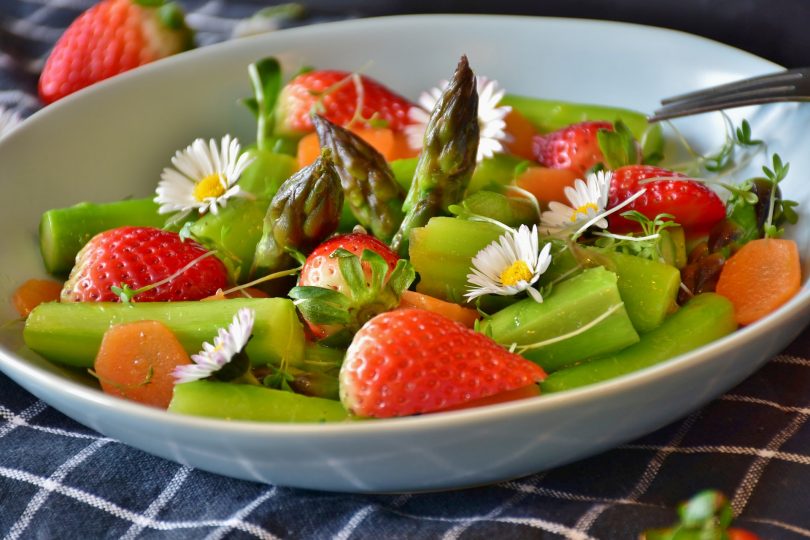 weisse Schüssel mit grünem Spargel, ganzen Erdbeeren und Gänseblümchen