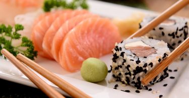 weisser Teller mit einer kleinen Wasabi Kugel, einem Maki mit weissem und schwarzem Sesamöl und Lach Sashimi