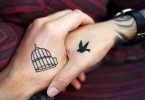 zwei Hände die sich die Hand geben eine hat einen offenen Vogelkäfig tätowiert und die andere eine fliegende Taube, und es schein als würde sie in den Käfig fliegen
