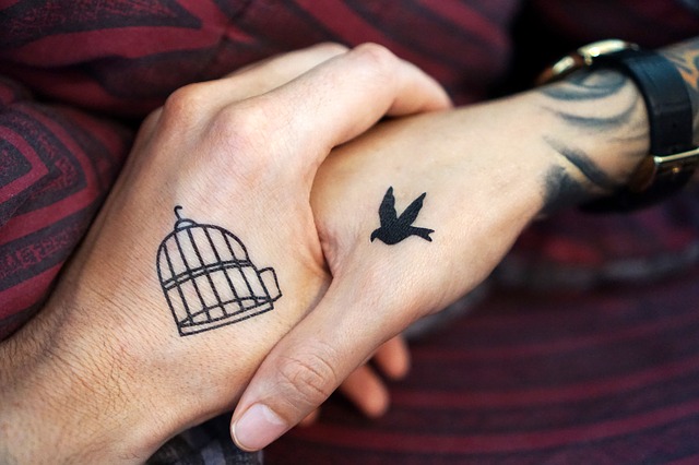 zwei Hände die sich die Hand geben eine hat einen offenen Vogelkäfig tätowiert und die andere eine fliegende Taube, und es schein als würde sie in den Käfig fliegen