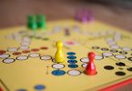 ein Mensch ärgere dich nicht Brettspiel mit verschiedenfarbigen Spielfiguren - gelb, rot, grün, lila- die auf dem dem Brett verteilt sind