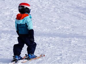 ein kleines Kind mit Helm und Skianzug das auf einer Schneepiste Ski fährt