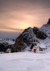 Sonnenuntergang in den Bergen, viel Schnee und zwei vereinzelte kleine Häuser