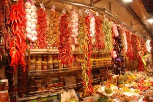 Ein Gewürzstand in der Boqueria mit einem Regal voller Gewürzgläser an der Wand und aufgehängte, getrocknete Paprika, Knoblauch, Chilis, und viel mehr