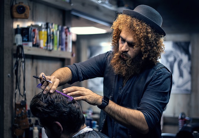 ein Friseur mit langem Bart, lockigen halblangen Haaren und schwarzem Hut der gerade einem anderen Mann die Haare schneidet