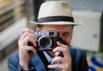 Ein junger Mann mit hellem Hut der gerade mit seiner Vintagekamera ein Foto von dir macht