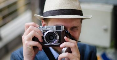 Ein junger Mann mit hellem Hut der gerade mit seiner Vintagekamera ein Foto von dir macht