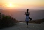 Eine Frau in der Position des Baums auf einem Berg während eines Sonnenuntergangs