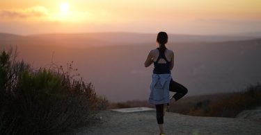 Eine Frau in der Position des Baums auf einem Berg während eines Sonnenuntergangs