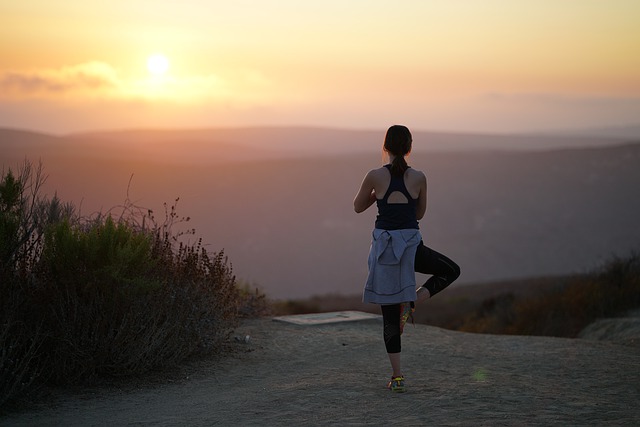 Eine Frau in der Position des Baums auf einem Berg während eines Sonnenuntergangs
