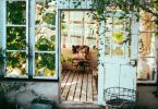 Einblick in deine Wintergarten einer Wohnung, eine weisse Holztür , ein Sessel, viele Hängepflanzen und Holzboden umgeben von Fenstern durch die viel Licht reinscheint