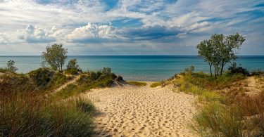 der zum Strand über eine Santdüne mit kleinen grünen Büschen an den Seiten