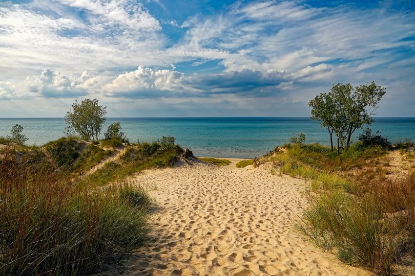 der zum Strand über eine Santdüne mit kleinen grünen Büschen an den Seiten