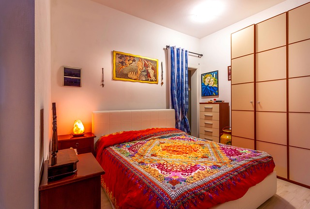 ein Schlafzimmer mit einer roten Decke und einem Mandala darauf, eine Himañayasalztischlampe und ein großer Schrank