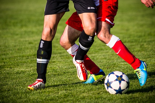 zwei Fußballspieler, einer in schwarz der andere in rot die im stadium auf grünem gras um den Fußball kämpfen