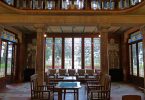 ein großer Saal mit großen Glasfenstern an allen Wänden, eine hohe gewölbte Decke und in der Mitte ein Holztisch mit vier Holztischen drum herum